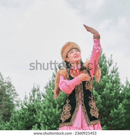 Close up of attractive smiling Asian girl in fur headdress and traditional festive Bashkir clothes dancing against background of coniferous forest and sky. Village festival, Siberia, Russia.Copy space