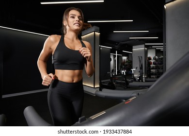 Close Up Of Attractive Young Sporty Woman In Black Sportswear Doing Cardio Exercise On Treadmill. Concept Of Training In Modern Gym And Pump Up Body.