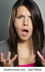 Close up of an attractive young woman with a horrified expression clenching her hands in frustration and desperation as she stares open-mouthed at the camera