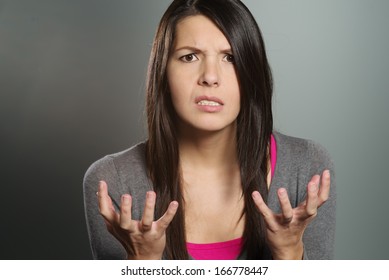 Close up of an attractive young woman with a horrified expression clenching her hands in frustration and desperation as she stares teeth-clenched at the camera