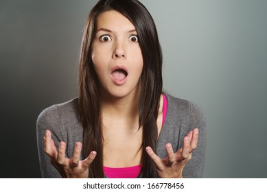 Close up of an attractive young woman with a horrified expression clenching her hands in frustration and desperation as she stares open-mouthed at the camera