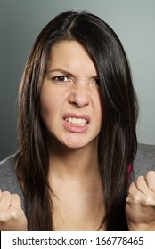 Close up of an attractive young woman with a horrified expression clenching her hands in frustration and desperation as she stares teeth-clenched at the camera
