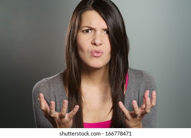 Close up of an attractive young woman with a horrified expression clenching her hands in frustration and desperation as she stares at the camera