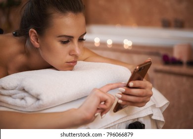 Close Up Of An Attractive Young Woman Lying On A Massage Table At The Spa Center Using Her Smart Phone Copyspace Technology Working Mobility Carrier Relaxing Connectivity Messaging Busy Hotel