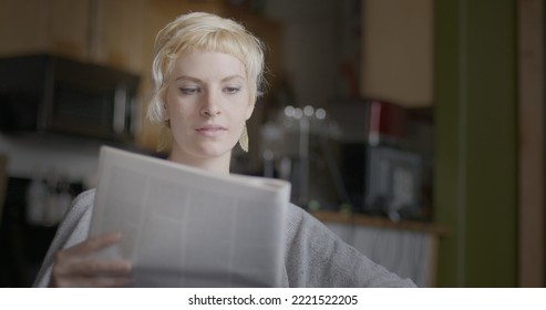 Close Up Of Attractive Young Woman With Short Blonde Hair Reading A Newspaper In Urban Loft Location