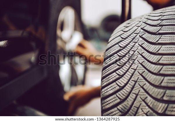 Close up of auto mechanic\
changing tire while crouching at workshop. Selective focus on\
tire.