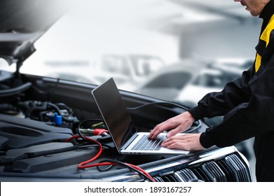 Close Up Of Auto Mechanic Hands Using Computer For Diagnostics Engine Working And Repairing Car In A Garage. Blur Repair Service In Background. Battery Check.