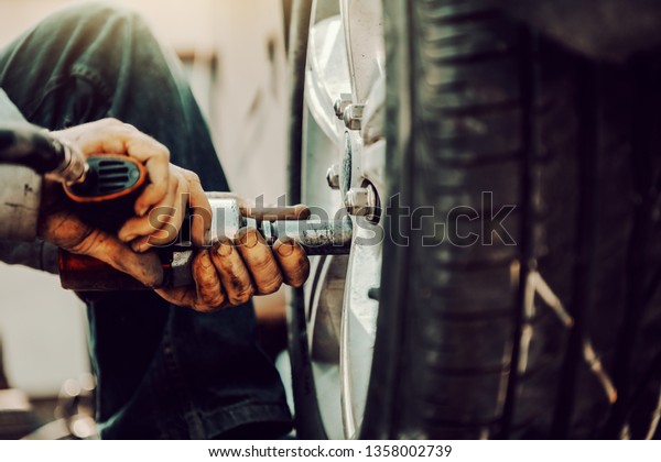 Close up of auto mechanic using tool to change\
tire while crouching at\
workshop.