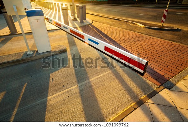 Close up\
of automatic boom barrier gate entrance illuminated by warm sunset\
light. Perspective view with long\
shadows