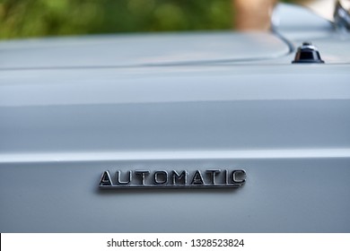 Close up of automatic emblem attached to the side of classic car front bonnet. The badge refer to automatic transmission version of sedan. Concept of change management and operating system.