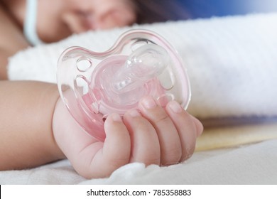 Close up of baby hands with pacifier, Silicone baby soother pacifier on white bed , Baby with a nipple