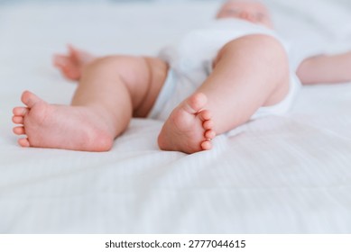 Close up of a baby's chubby legs resting comfortably on a white bed in a diaper. Authentic domestic child care and healthy physical development concept.