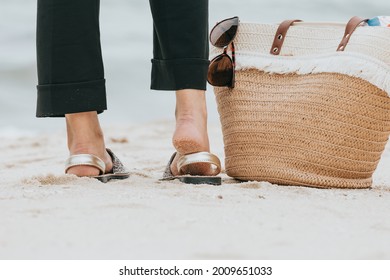 Close up of the back of a woman’s feet with a beach bag near and a pair of sunglasses - Powered by Shutterstock