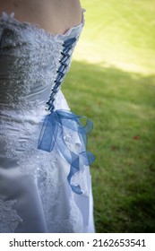 Close Up Of The Back Of A Formal Wedding Gown With The Dress Laced Up And A Bow Tied With Blue Ribbon And Green Grass Background