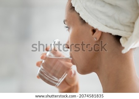 Close up back side view happy peaceful young hispanic woman drinking glass of fresh filtered mineral pure water after morning shower, enjoying daily healthcare habit, sipping aqua, stay hydrated.