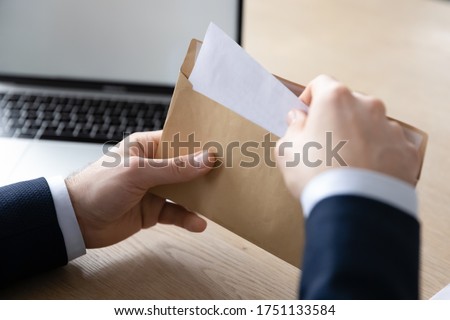 Close up back view of businessman sit at office desk open envelope with postal paper document, male employee unpack post paperwork letter or correspondence with decision notification or law order