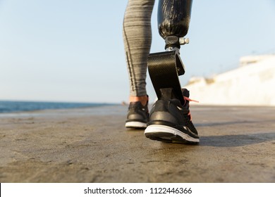 Close up back view of disabled athlete woman with prosthetic leg walking at the beach - Powered by Shutterstock