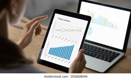 Close up back view of female accountant work on electronic gadgets prepare financial report on tablet and laptop. Businesswoman use devices manage finances, analyze diagrams statistics in office.