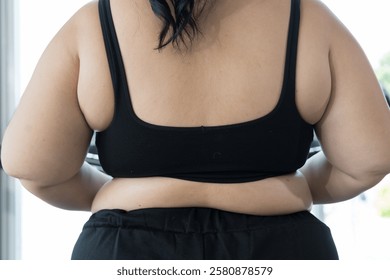 Close up of back view of plus size woman in black sportswear during workout in fitness gym. Back view of oversize woman exercise in gym