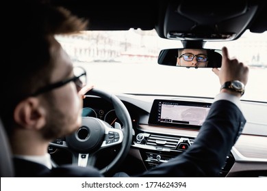 Close up back view portrait of man in specs adjusting rearview mirror while sitting in his car, selective focus