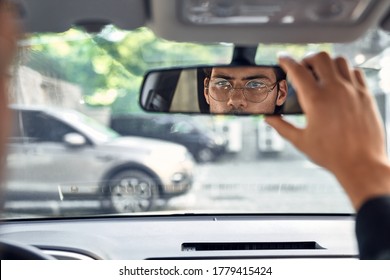 Close up back view portrait of man in specs adjusting rearview mirror while sitting in his car, selective focus.