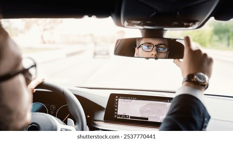 Close up back view portrait of man in specs adjusting rearview mirror while sitting in his car, selective focus