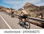 Close up back view of two professional cyclist racers. Cycling group training on a road bicycles at sunset in the mountains. Training for competition. Practicing cycling on open country road. Spain.