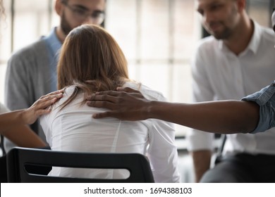 Close up back view unhappy woman with supporting diverse people at therapy session, touching shoulders, sitting in circle. Stressful businesswoman getting psychological help, trust and support.