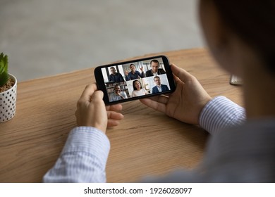 Close Up Back View Of Woman Sit At Desk Talk On Video Call With Multiracial Colleagues On Smartphone. Female Employee Have Webcam Digital Online Meeting With Coworkers On Cell. Virtual Event Concept.