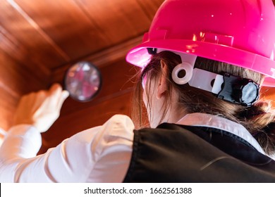 close up back view of women inspector during home air quality inspection, looking for molds or fungi problems on a wooden roof using magnifying glass