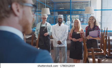 Close Up Back View Of Young Cafe Manager Instructing Staff Before Opening. Small Business Owner Giving Instructions For Restaurant Workers On First Day At Work. Coffee Shop Staff Briefing