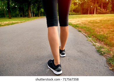 Close Up From The Back Of A Young Blonde Woman Running Away From The Camera On The Road In A Park
