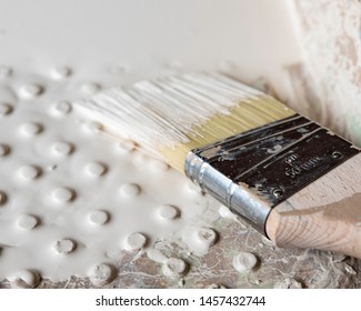 Close up background image with shallow focus of a two-inch trim paint brush loaded with a light cream colored paint in a paint tray.