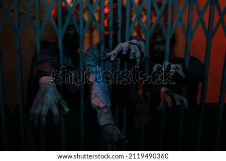 Close up background image of zombie hands reaching out through door in dark hallway, copy space