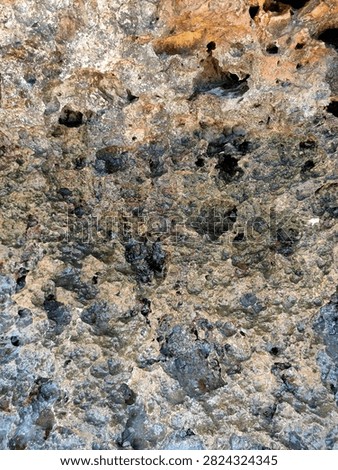 Close up background of sharp, weathered volcanic rock cliff with dark porous hollows and bumpy mineral texture on the seashore.