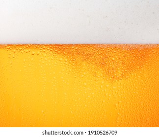 Close up background texture of pouring lager beer with bubbles and froth in frosty glass with drops, low angle side view - Shutterstock ID 1910526709