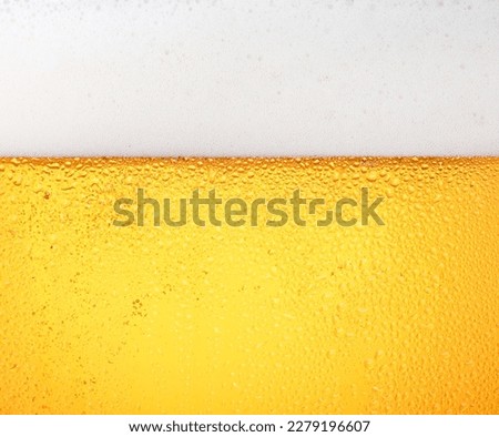 Close up background texture of pouring lager beer with bubbles and froth in frosty glass with drops, low angle side view