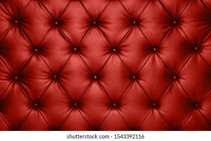Close up background texture of scarlet red capitone genuine leather, retro Chesterfield style soft tufted furniture upholstery with deep diamond pattern and buttons