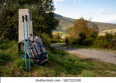 Close up of backpack with walking stick and Camino de Santiago sign, with pilgrim walking along the path, symbol of pilgrimage and walking on the way to Santiago