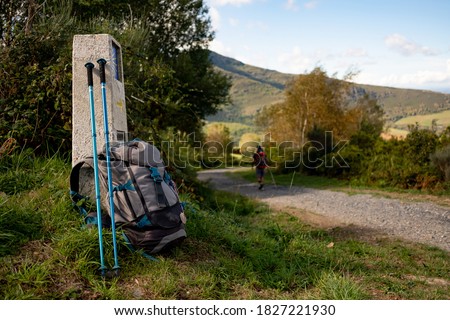Close up of backpack with walking stick and Camino de Santiago sign, with pilgrim walking along the path, symbol of pilgrimage and walking on the way to Santiago