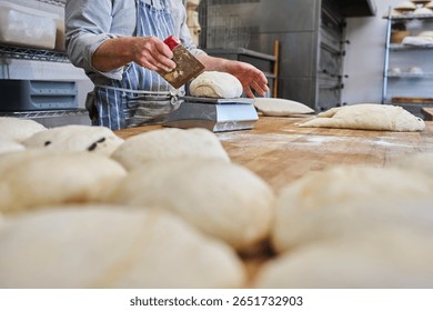 Close up of baker cutting and weighing batch of dough to make individual loaves in bakery                               