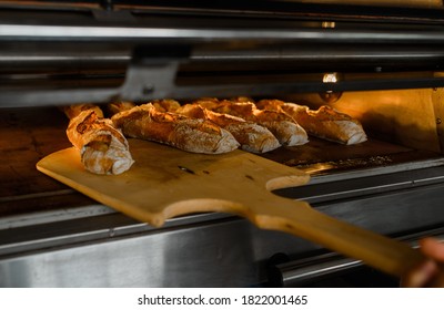 Close up of baker is taking off from oven the french baguette bread with wood peel at baking manufacture factory. French baguette bread bakery factory concept. - Shutterstock ID 1822001465