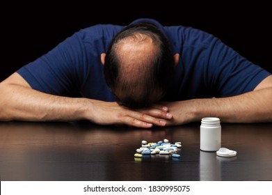 Close Up Of A Bald Man Depressed By The Ineffectiveness Of Pills To Prevent Hair Loss On A Dark Background