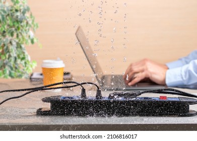 Close up of a bank of plugs on a desk with water leaks falling next to a man working in danger of electrocution at home or office