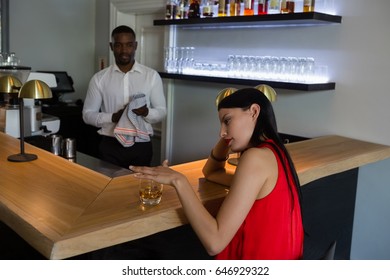 Close Up Of Bar Tender Looking At Depressed Young Woman Sitting By Counter