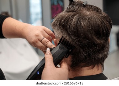 Close up of a barber using a red electric hair trimmer clipper to cut a man hair, precise hair cutting technique performed in a professional barbershop setting during a haircut session at the salon today