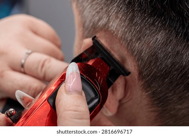 Close up of a barber using a red electric hair trimmer clipper to cut a man hair, precise hair cutting technique performed in a professional barbershop setting during a haircut session at the salon today