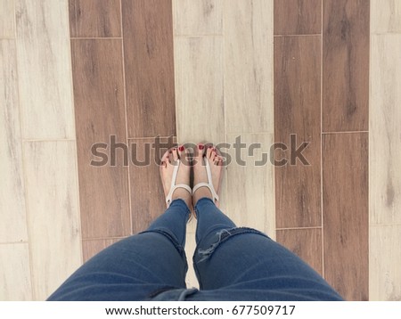 Close up of Bare Feet with Red Nail in Sandals and Blue Jeans Woman On The Tile Background Great For Any Use.