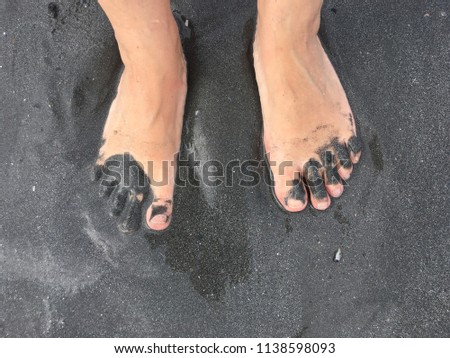 Close up of barefoots buried on dark gray beach sand on the sea shore