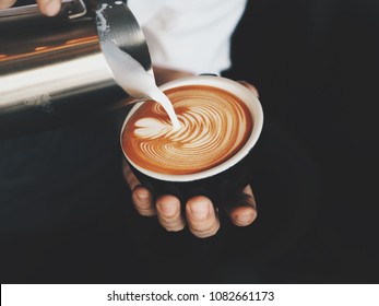 Close up barista hands pouring warm milk in coffee cup for making latte art.